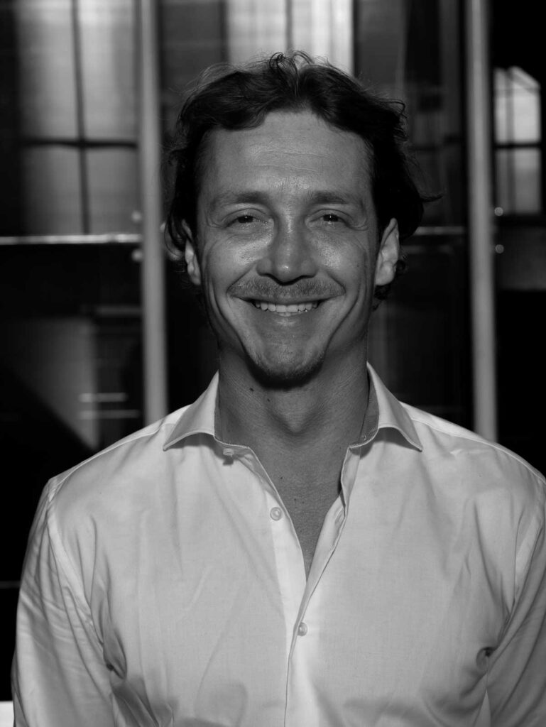 Smiling man in a white shirt against a blurred background, conveying a professional and approachable demeanor.